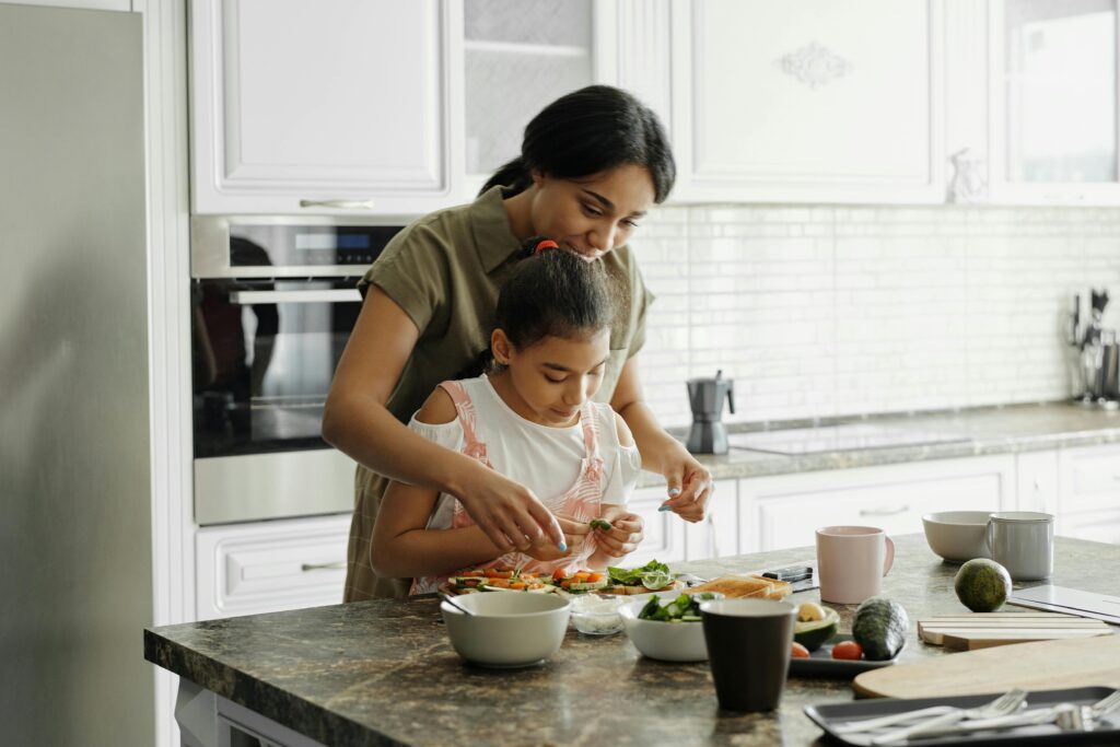 A woman and child prepare food together in a modern kitchen, surrounded by fresh ingredients on a countertop.