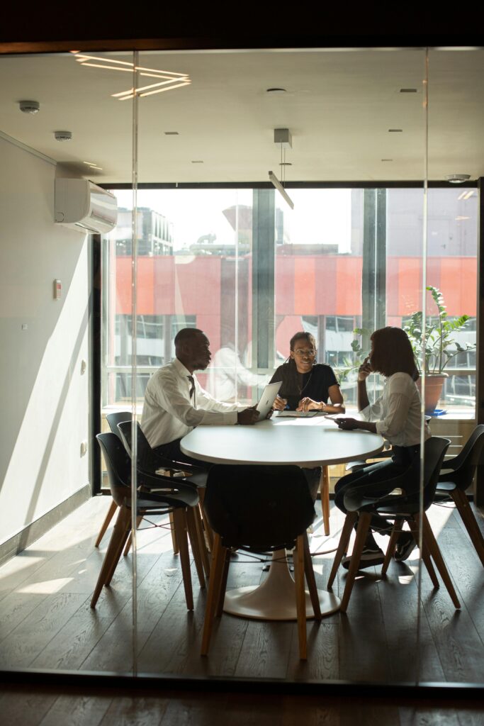 Three people having a meeting in a modern glass-walled office with natural light.