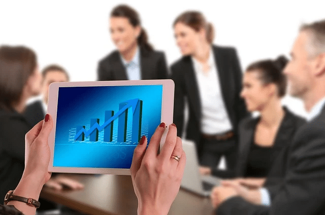 Businesspeople having a meeting, with a person holding a tablet showing upward financial growth, related to secondary sale law firms.