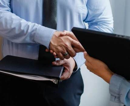 Two people in formal attire shaking hands with documents, discussing vendor financing for selling a business.