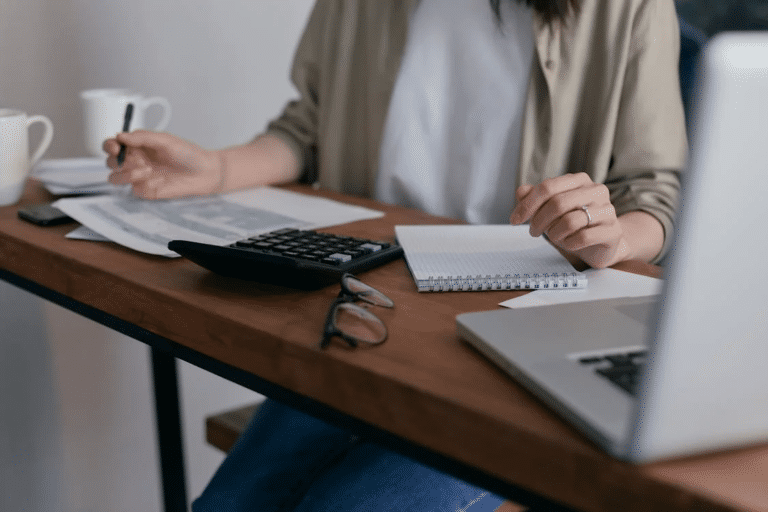 Person analyzing documents with calculator, notepad, and laptop, highlighting potential tax implications when selling a business.