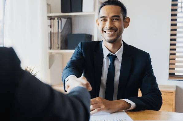 Smiling businessman in suit shaking hands, discussing how outgoings influence the purchase price in a sale of a business law firm.