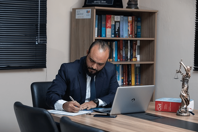 A lawyer in an office writes on paper while preparing business sale documents for a law firm, with law books in the background.