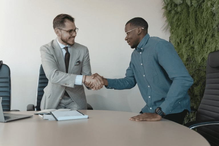 Two men shaking hands in an office, illustrating a successful agreement when selling a business and finding the right buyer.