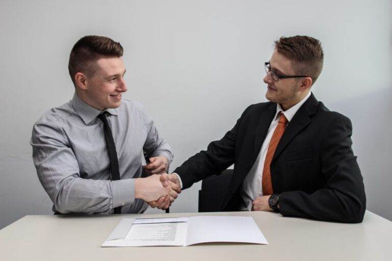 Two businessmen shaking hands across a table with documents, illustrating why goodwill is important for businesses and law firms.