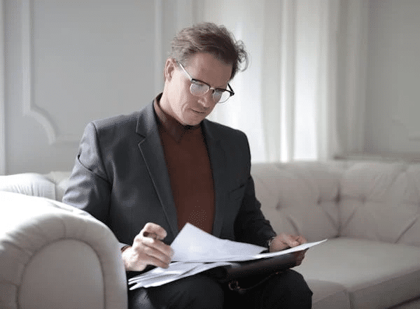 Man in a suit reviewing documents on a sofa, representing legal requirements for buying a medical practice in NSW.