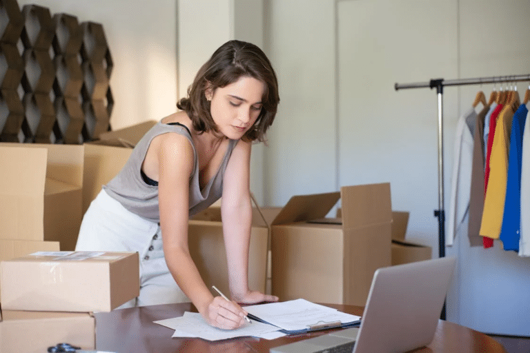 Woman reviewing documents to buy an ecommerce business, surrounded by boxes and clothing on a rack.