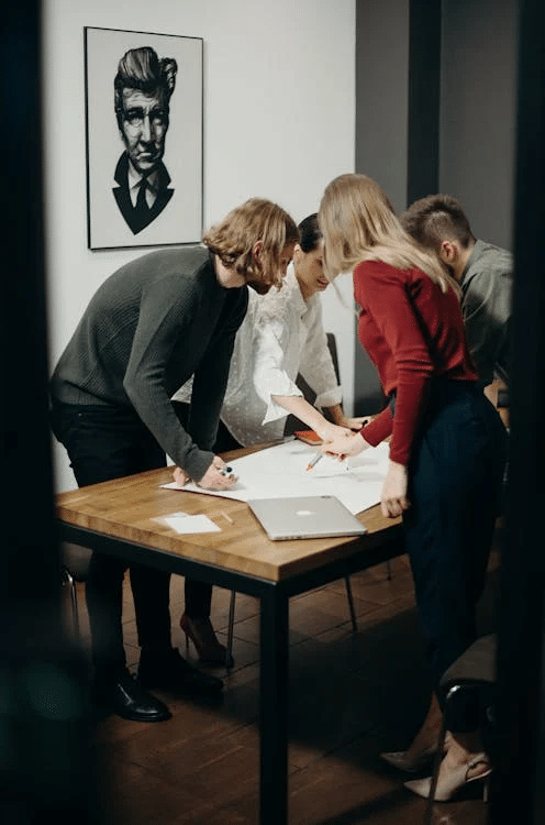 Employees gathered around a table discussing business sale implications.