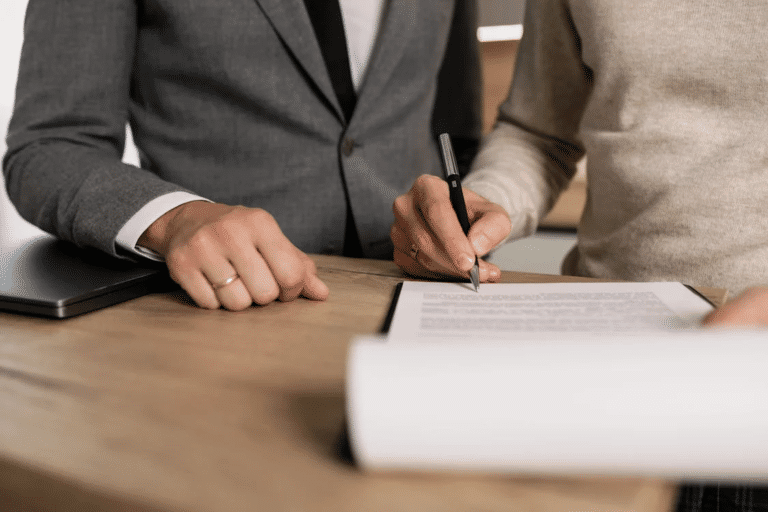 Two people reviewing and signing a heads of agreement document at a wooden desk.