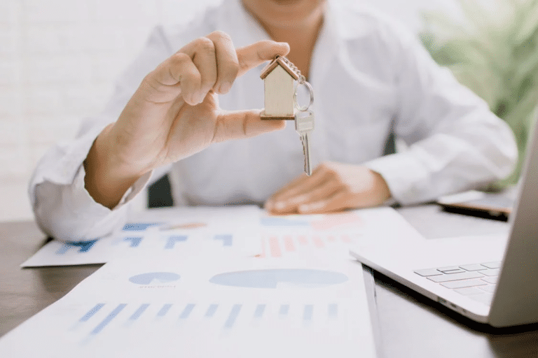 Person holding house key over charts, symbolizing buying a real estate agency.