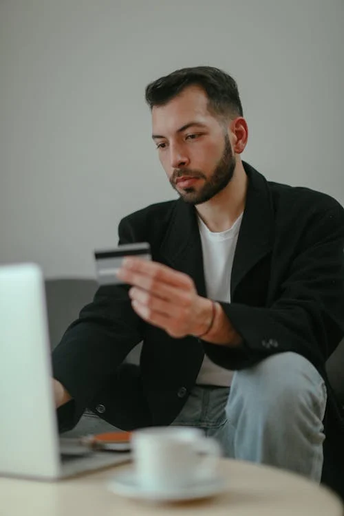 Man considering personal guarantees in business, holding credit card, with focused expression in front of laptop.