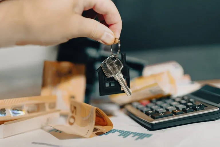 Hand holding house key over currency and calculator, symbolising distressed asset sale process and opportunities in NSW.
