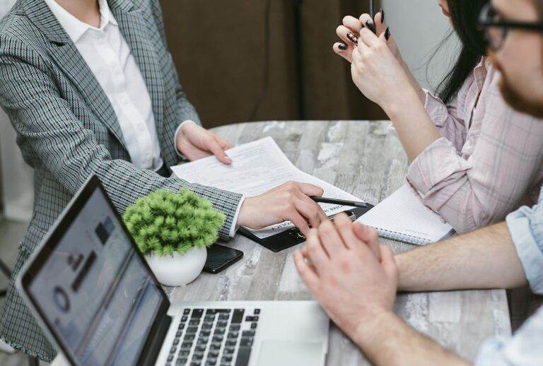 Business meeting discussing how to buy an RTO business in NSW, focusing on legal requirements and due diligence, with documents and laptops on a table.