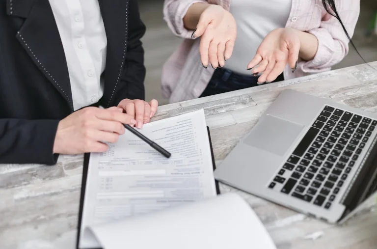 Two people discuss legal documents for selling a childcare centre in NSW, with a laptop on the table.