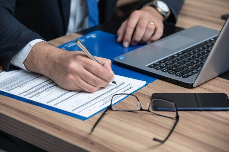 Person signs legal documents at a desk with a laptop, highlighting considerations for buying a media agency in NSW.