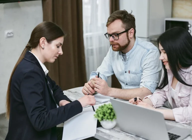 Three people discuss legal requirements for selling an eCommerce business in NSW, with documents and a laptop on the table.