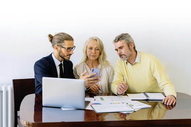 Three people discussing intangible assets in business acquisitions, a legal guide, around a table with papers and a laptop.