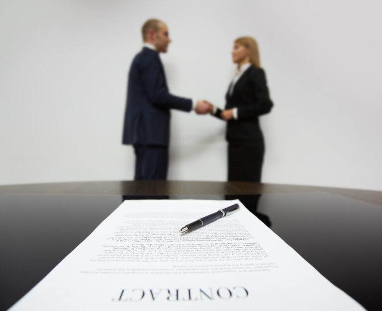 Contract on table with pen; blurred background shows two people shaking hands, illustrating franchising vs licensing.