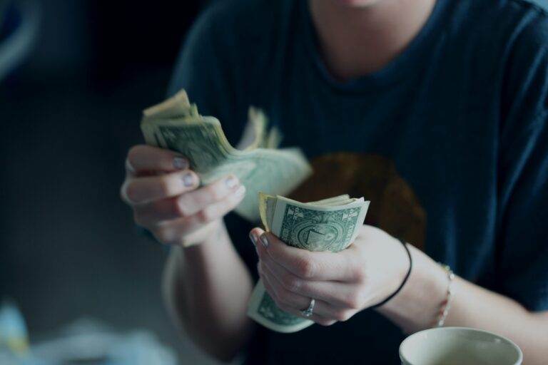 Person counting dollar bills, highlighting earn-out agreement risk management strategies.