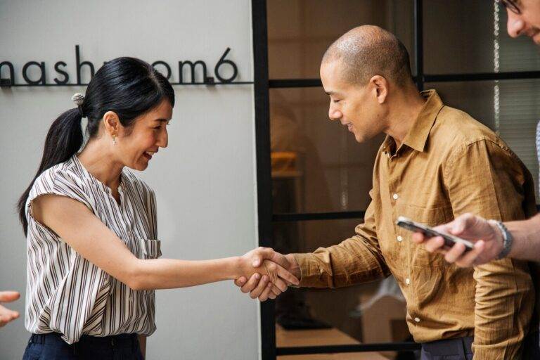 Business handshake agreement on warranties to avoid selling a business, two people smiling in an office setting.