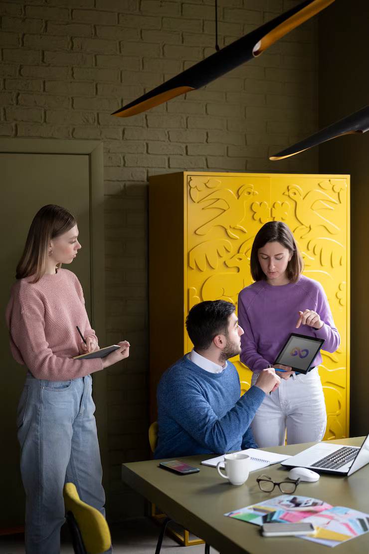 Team discussing a business rebrand guide around a table with laptop and tablet, in a modern office setting.