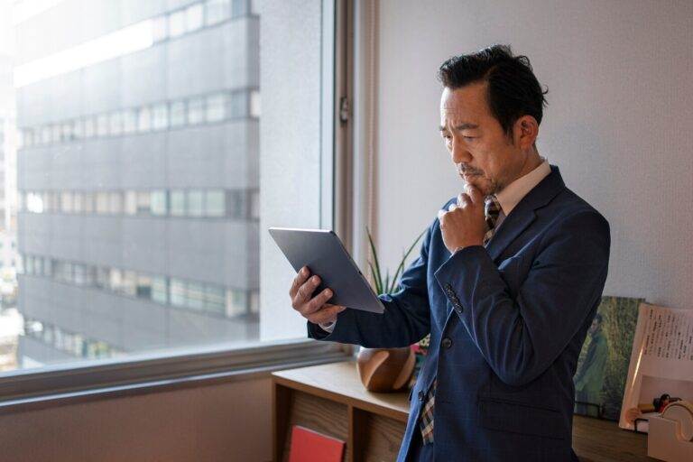 Man in suit analyzing tablet, indicating concern over business purchase red-flag near city window.